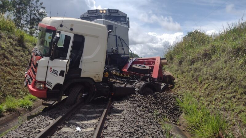 (ASSISTA AO VÍDEO) Caminhão que transportava retroescavadeira é atingido por trem